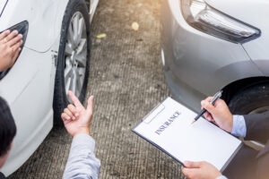 Insurance agent writing on clipboard while examining car after accident claim being assessed and processed